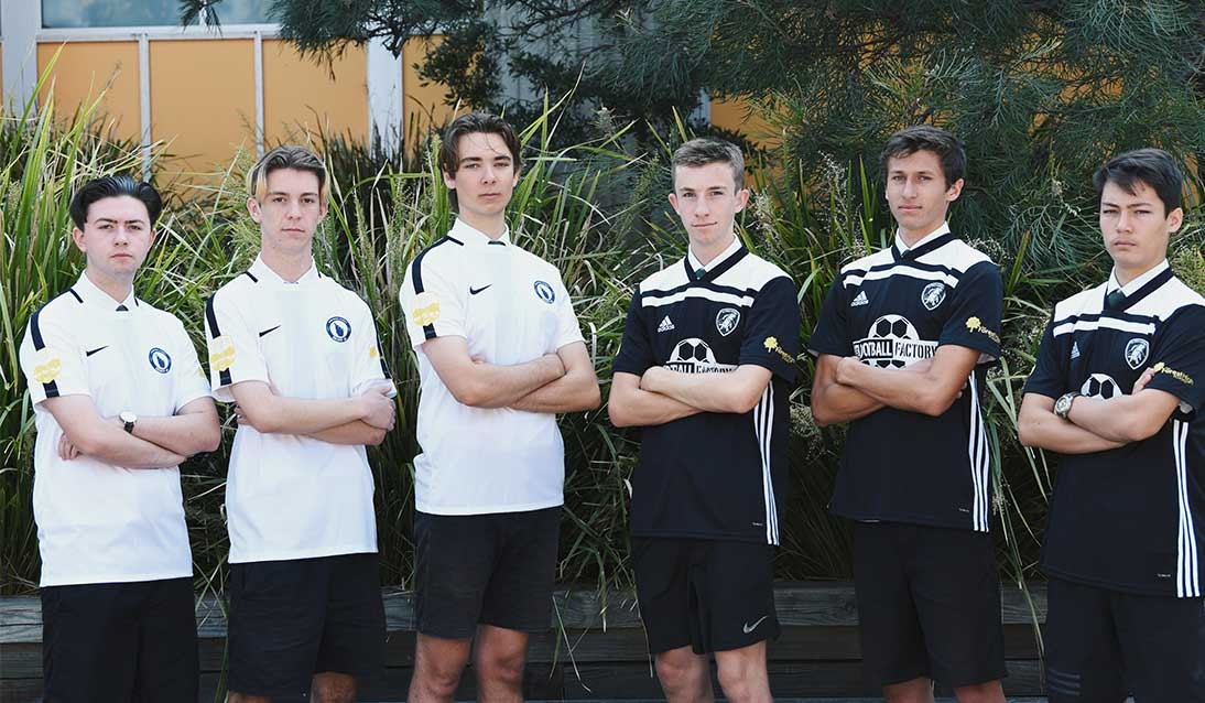 Six boys from two soccer teams stand looking at camera with arms crossed.