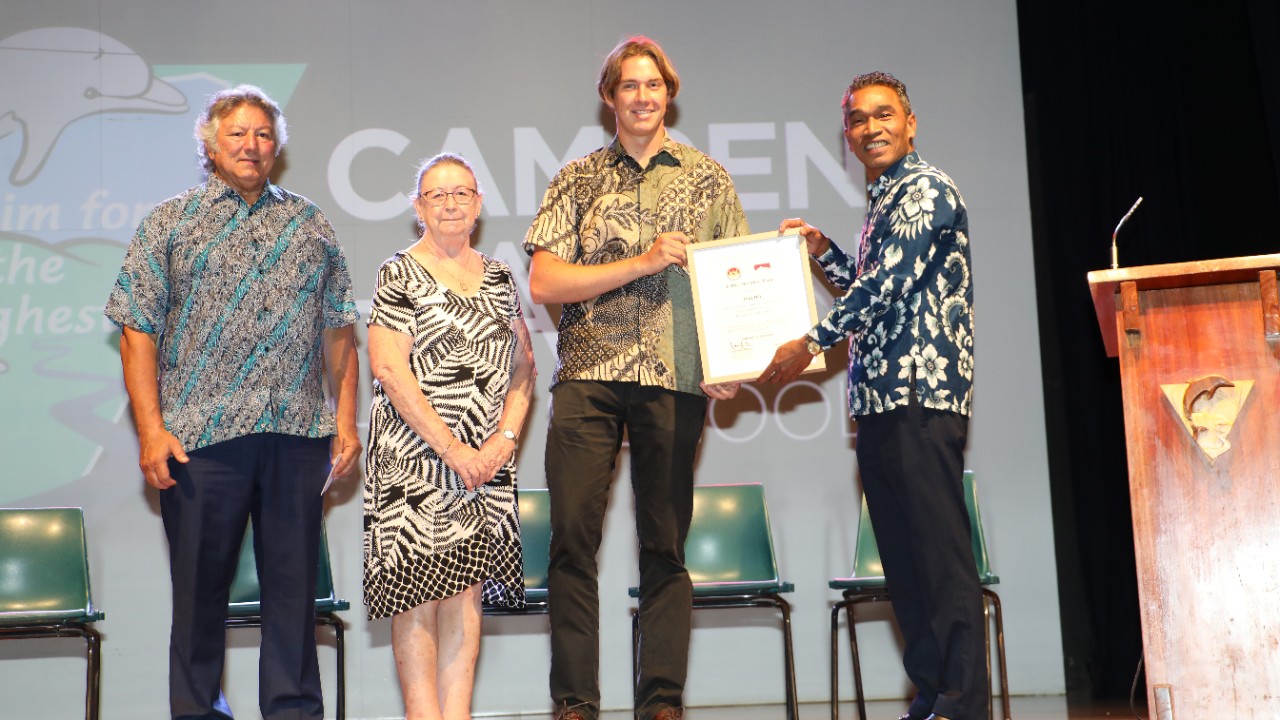 Four people standing on a stage facing the camera. Two of the people are holding a certificate between them.