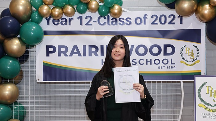 A young girl stands in front of a high school graduation sign