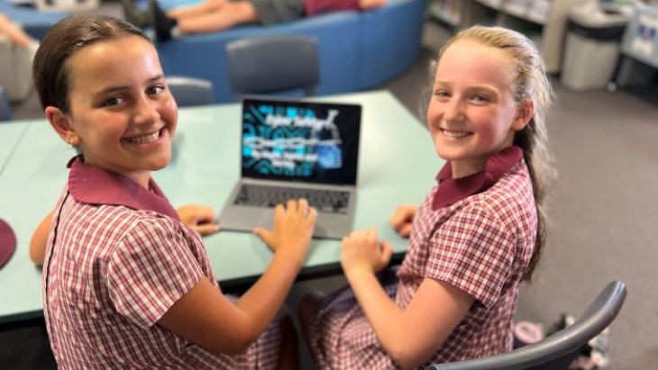 Two female students smiling and working on a laptop.