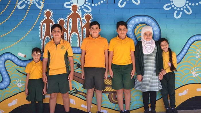 Six children stand in front of an Aboriginal-themed mural