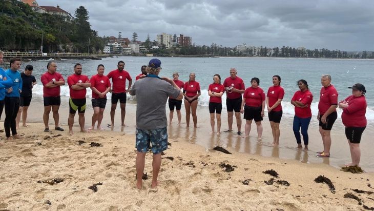 People wearing red rash shirts standing on a beach.