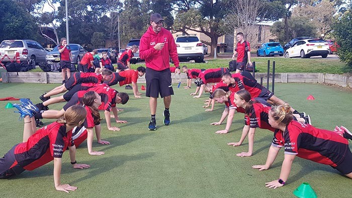 A coach stands in the middle of two lines of students doing pushups