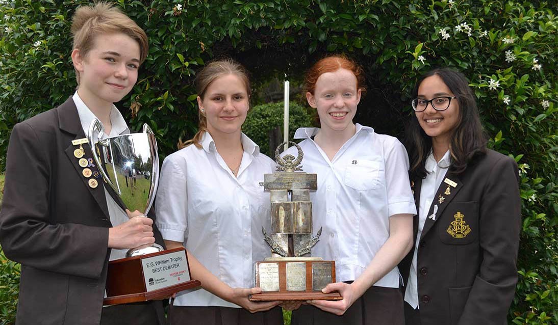 Four young girls face the camera holding two trophies
