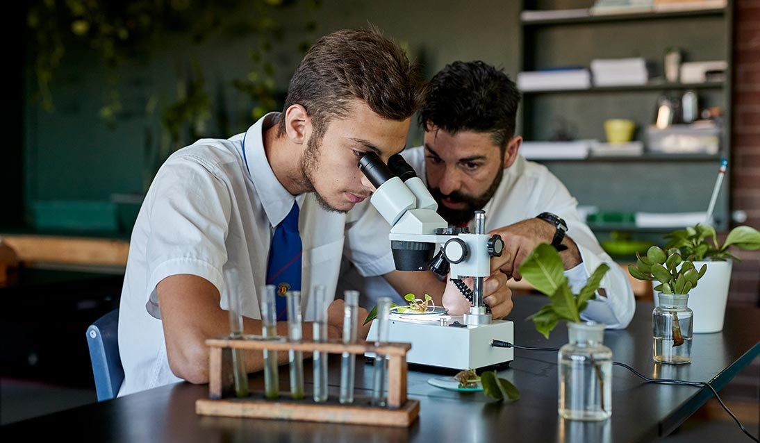 A high school student and teacher look through a microscope at scientific samples.