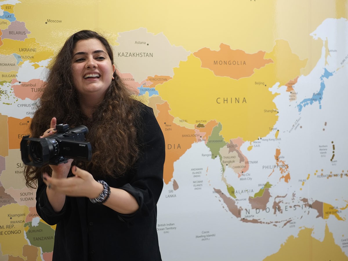 Joelle holding a camera, standing in front of a world map