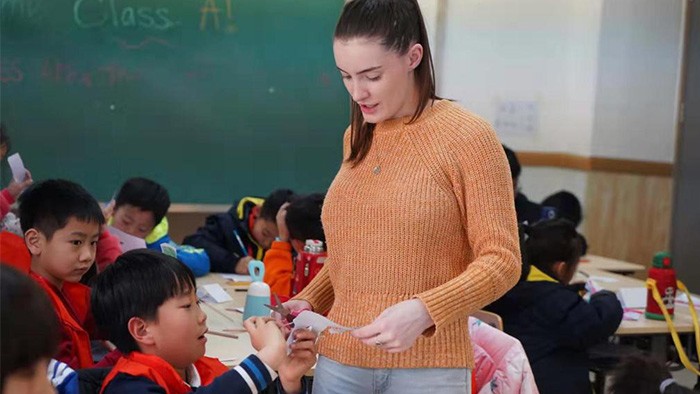 A young teacher in a classroom with Chinese students.