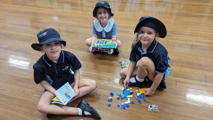 Students sitting on a wooden floor playing with Lego.