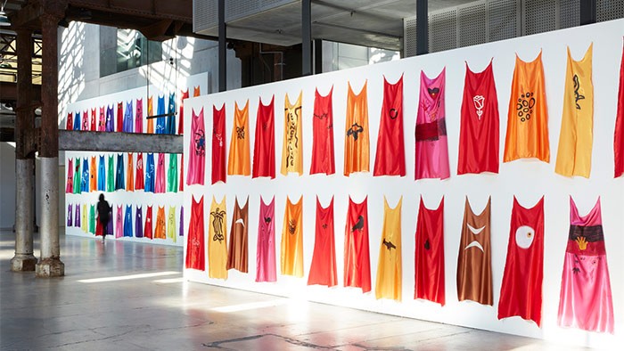 Rows of capes hanging on a white board as part of an exhibition.