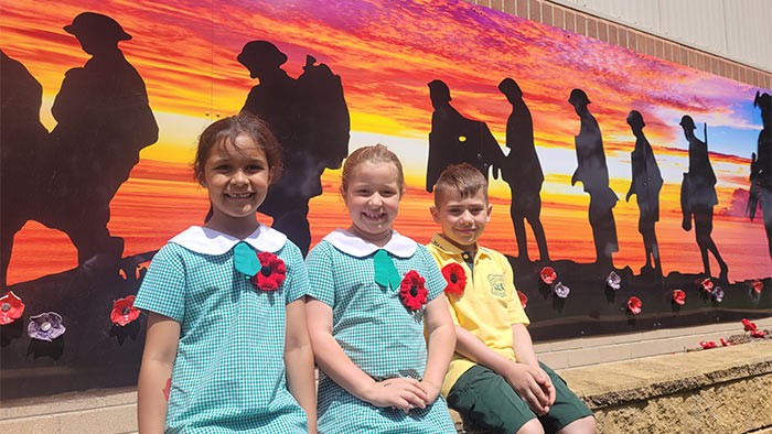 three children stand in front of a mural showing men marching off to war