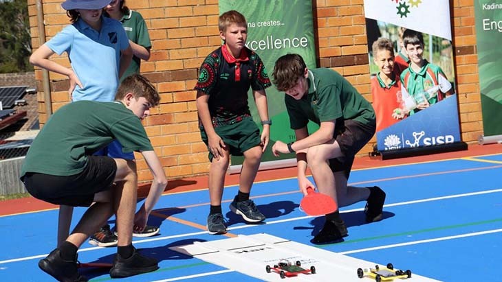 Students with toy cars on a track.