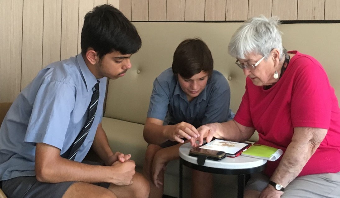 Two young boys sit with an elderly woman showing her how to use an iPad