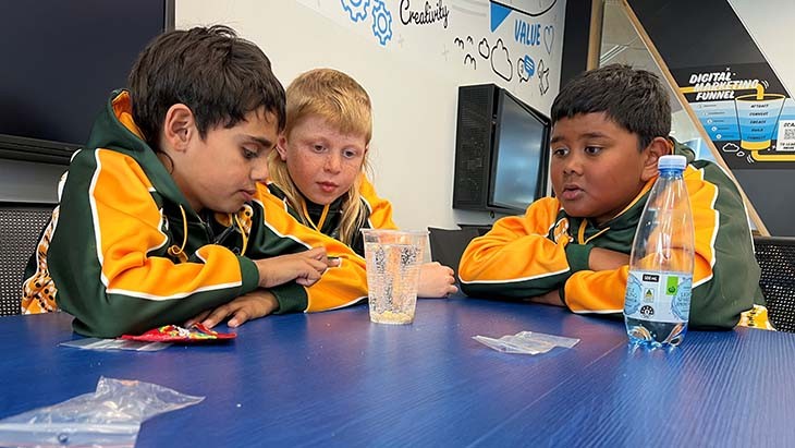 Three students watch a glass of water.