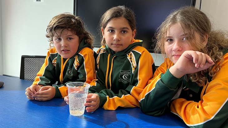 Three students pose for a photo with a glass of water.