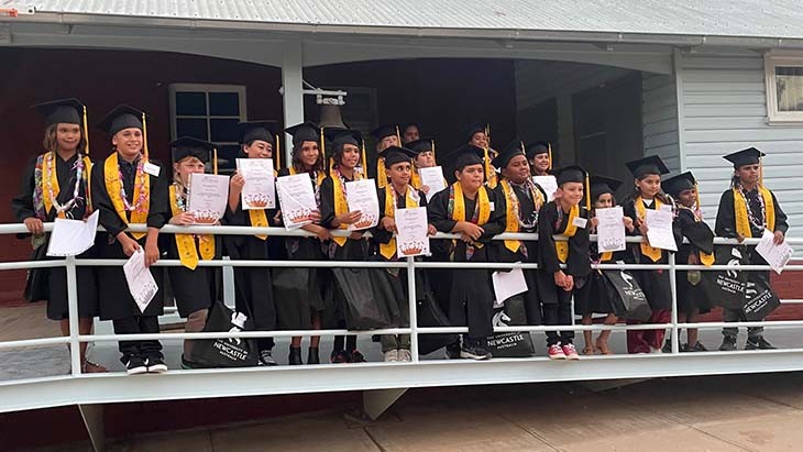Students pose for a photo wearing graduation gowns and boards.