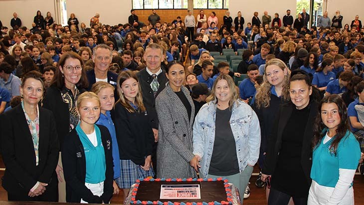 Students, staff and community members cutting a cake.
