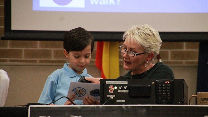A young boy speaks through a microphone held by his teacher.