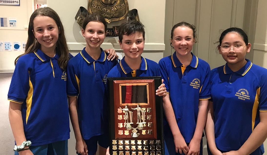 Five students wear blue uniform and hold a trophy.