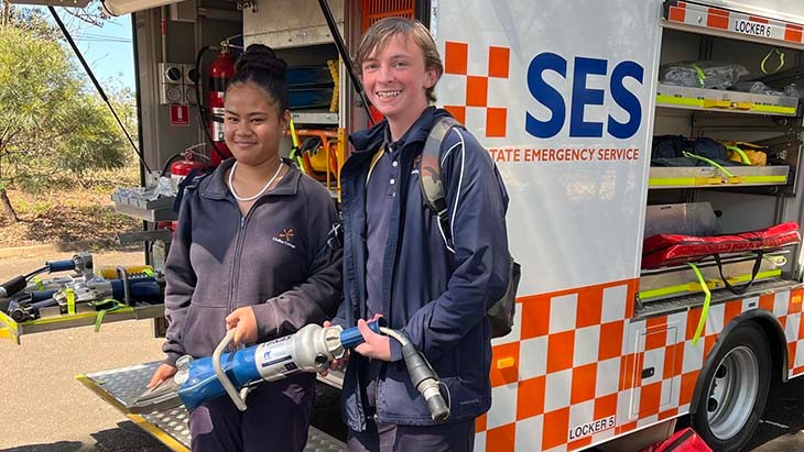 Two students holding the jaws of life in front of an SES vehicle.