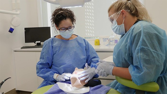 Two women practice dental hygiene on a dummy.