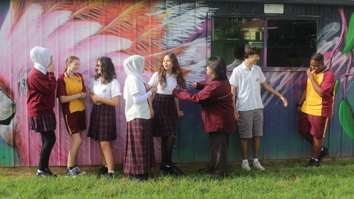 Students standing chatting in front of a mural on a shed.