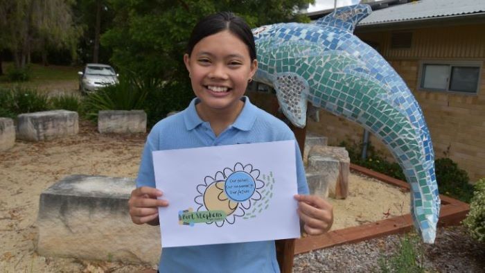 Young girl student smiling and holding up a picture with dolphin statue in the background