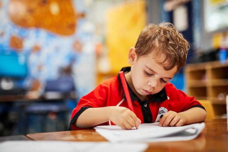 boy in black and red shirt writing at desk 