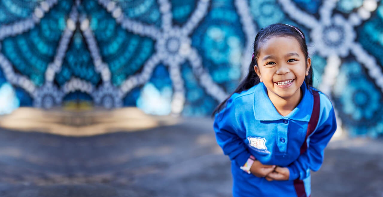 Girl standing in blue uniform in front of large mural. 