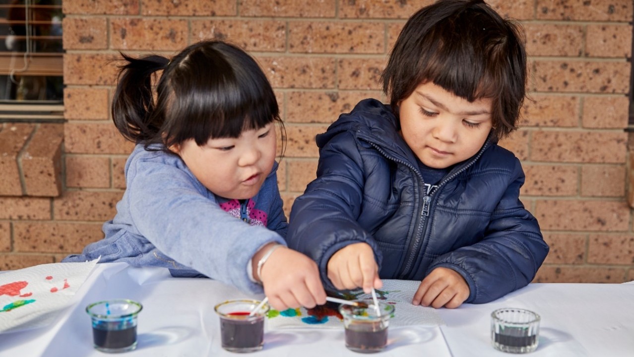 Two pre-school aged children working on a craft table.