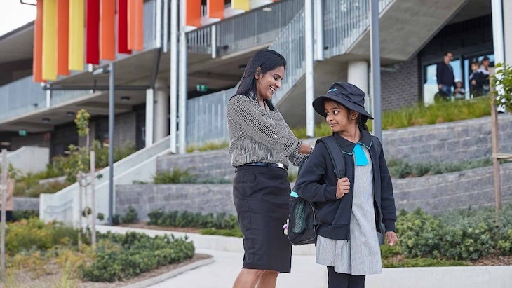 Parent standing in front of primary school with primary school student opening up her bag