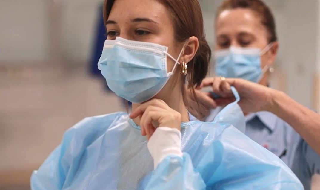 Nursing student wearing mask getting surgical gown tied up