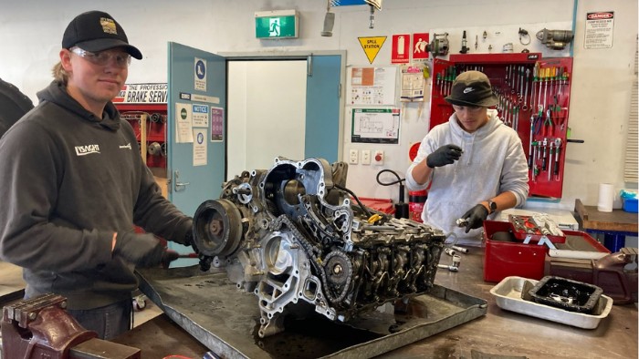 Two teenage boys in automotive mechanic workshop