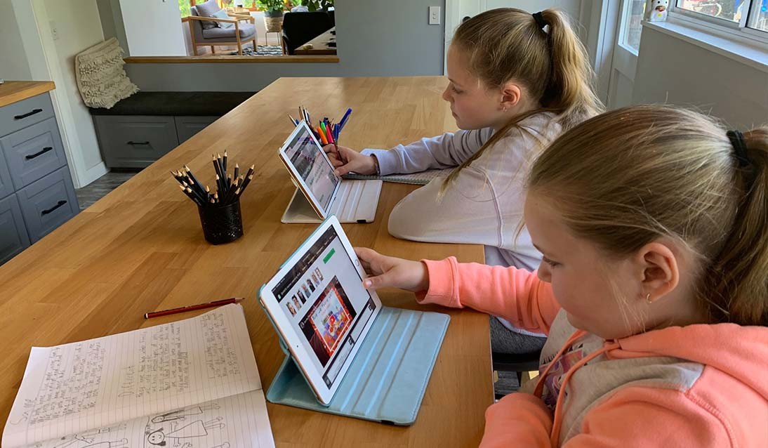 Two girls sit a a dining table using iPads.
