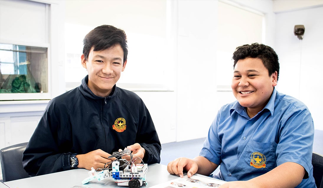Two high school boys sit in a classroom building robots.