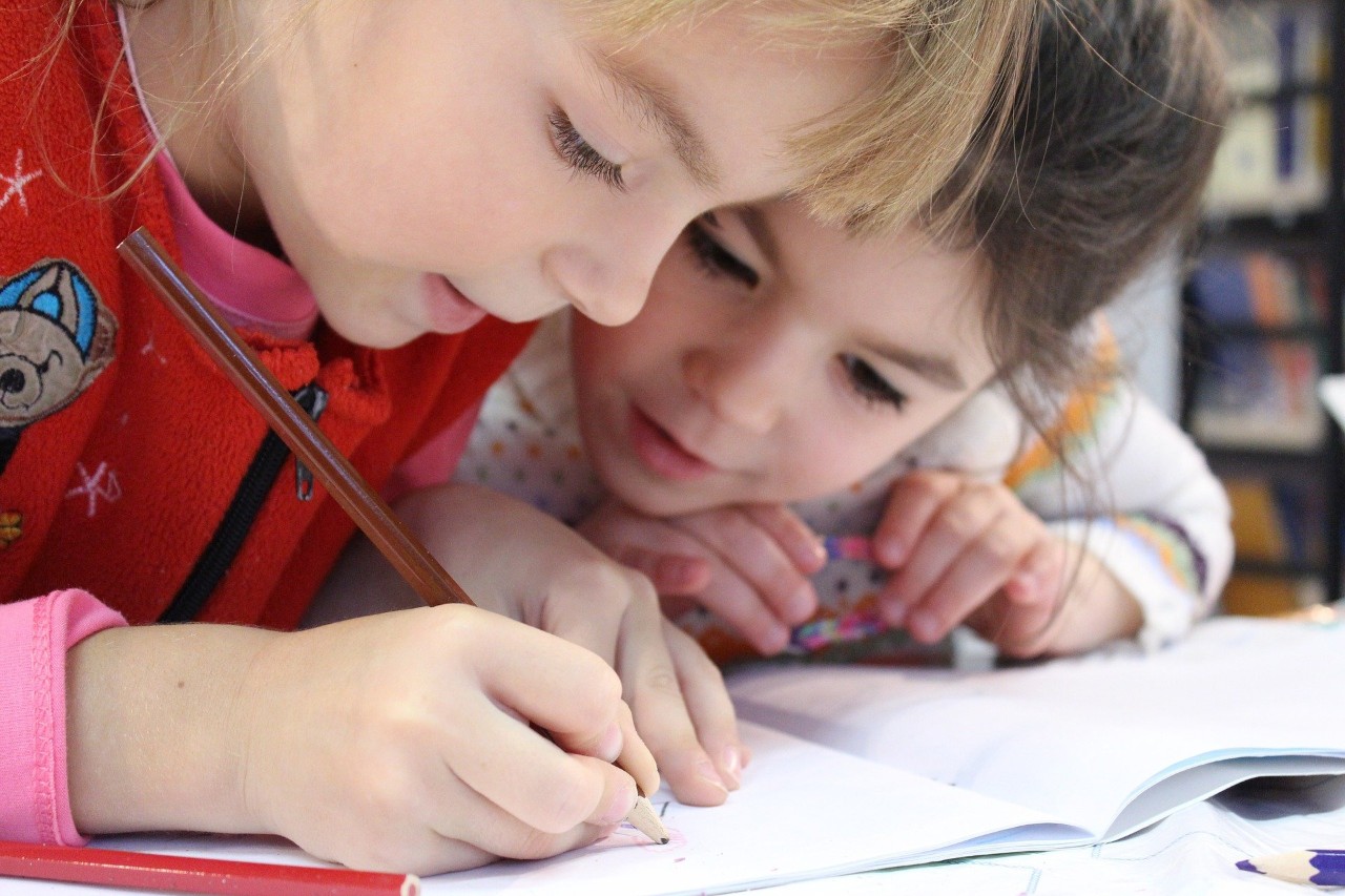 Two female children looking at a note book. One child is holding a pencil.