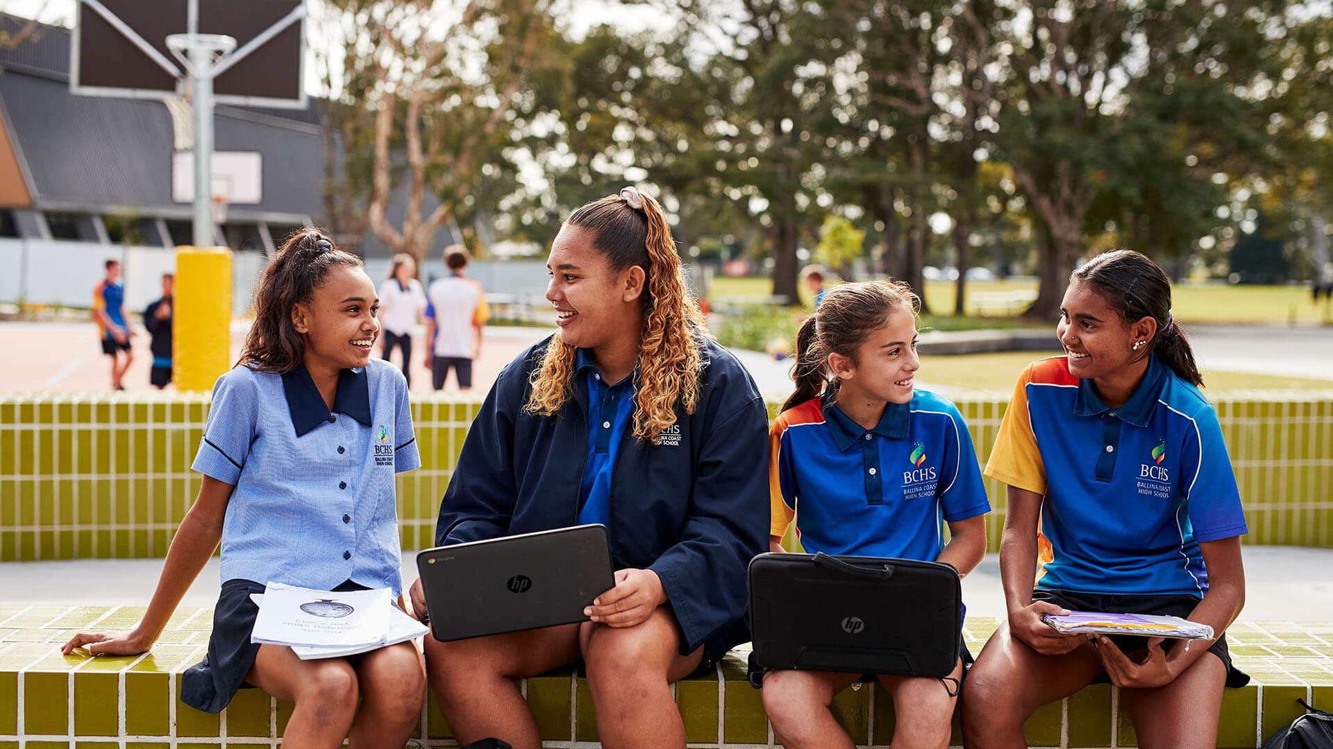 High school students sitting in playground talking and using computers