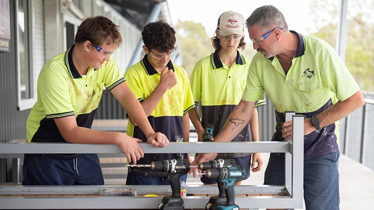 A group of young male apprentices with supervisor explaining drilling procedures.