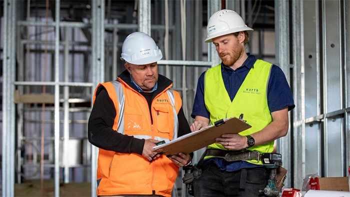 Male construction apprentice with supervisor looking at building plans.