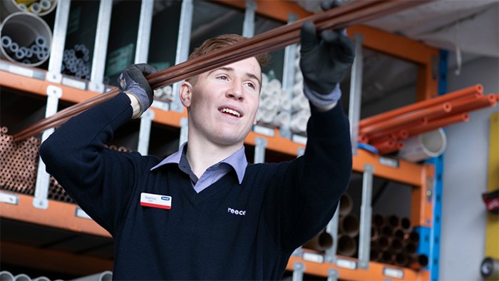 Male VET apprentice in hardware store holding copper pipes.