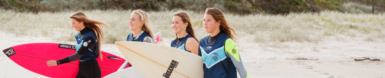 High school students on beach walking with surfboards