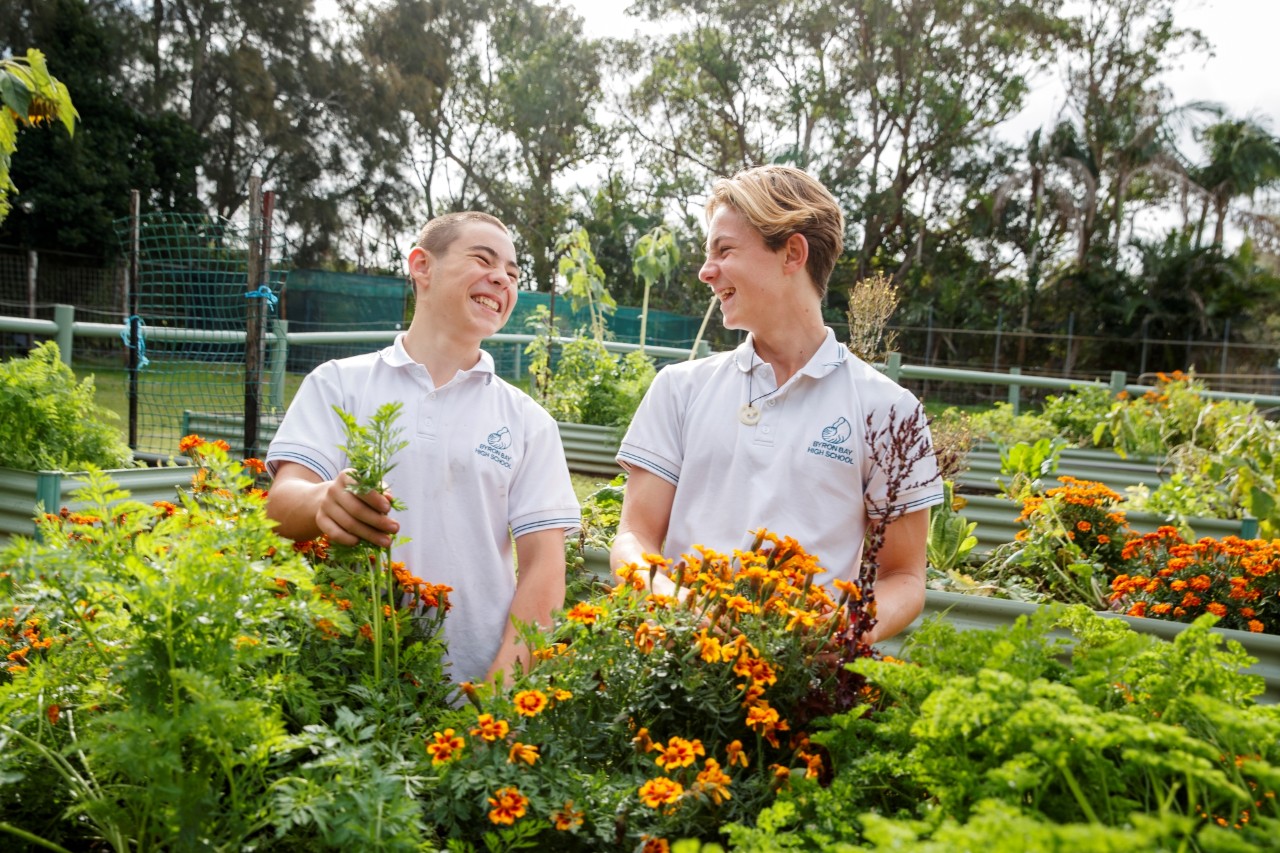 Two high school students digging in a veggie patch outside and smiling at each other