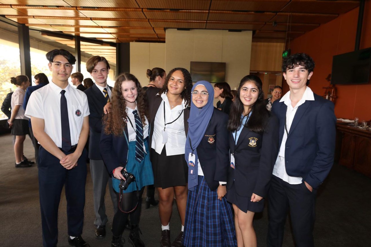 Group of students standing in NSW Parliament House with two students seated at the front looking towards the camera.