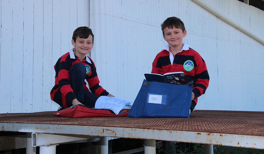 Two boys wearing red and black stripe shirts sit on a metal landing reading books.