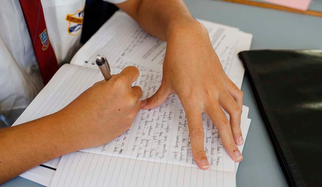 Close up of a student's hands holding a pen an writing in an exercise book. 