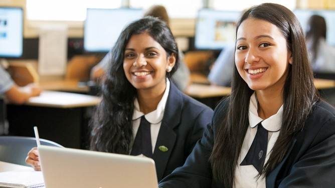 Two female students sit at a desk in a classroom