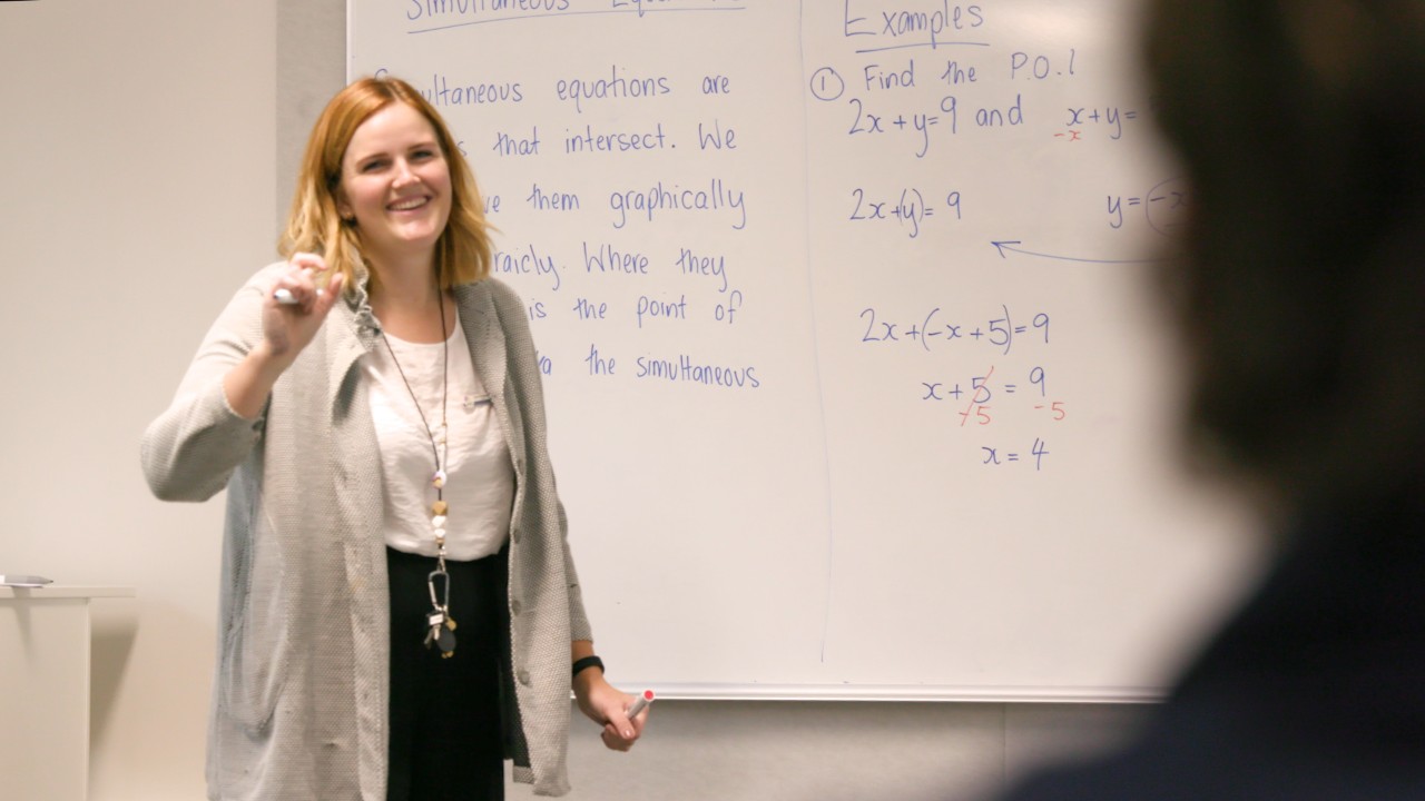Smiling teacher standing in front of a whiteboard holding a marker