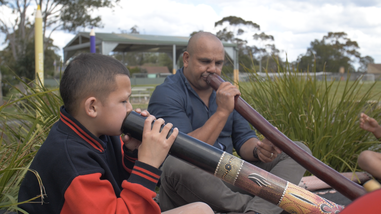 Male teacher playing the didgeridoo with a male student