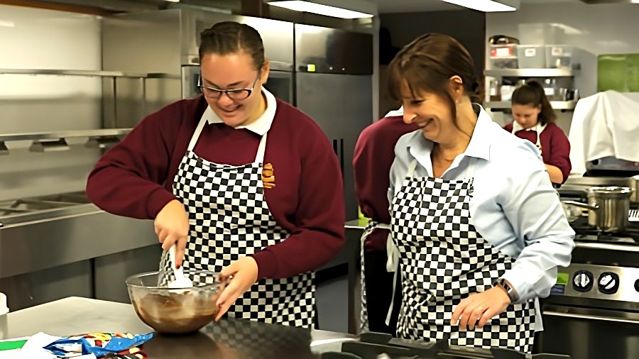 Female teacher standing next to female student in kitchen classroom