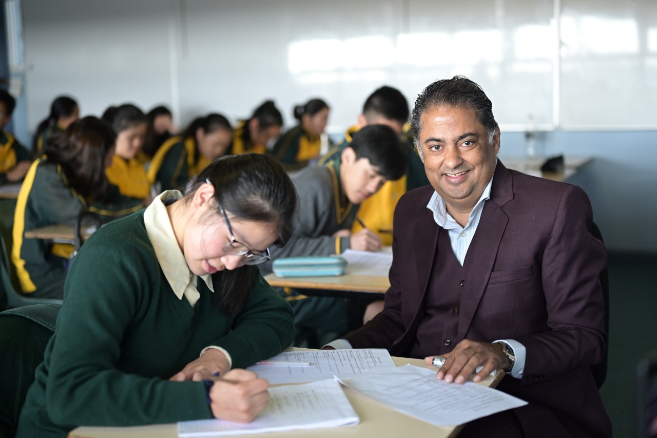 Male teacher sitting with female student smiling at camera
