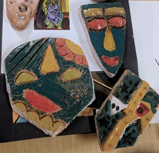 Examples of students ceramic masks green masks with yellow, red and orange features.